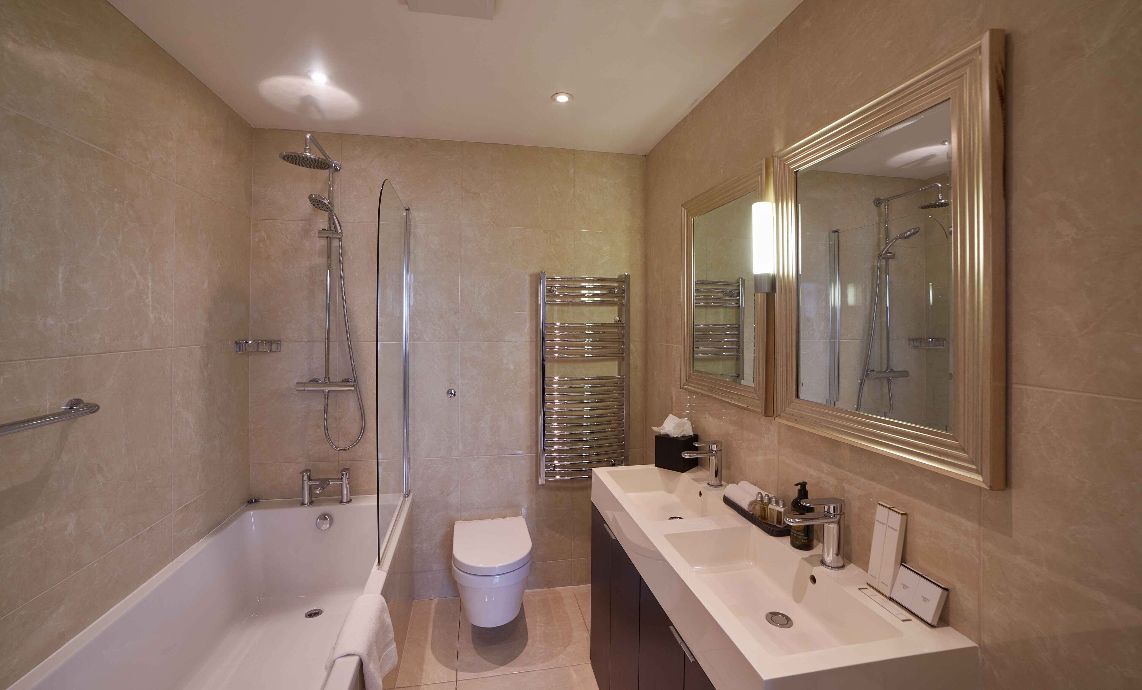 A modern bathroom with a bathtub, shower, toilet, and a large mirror.