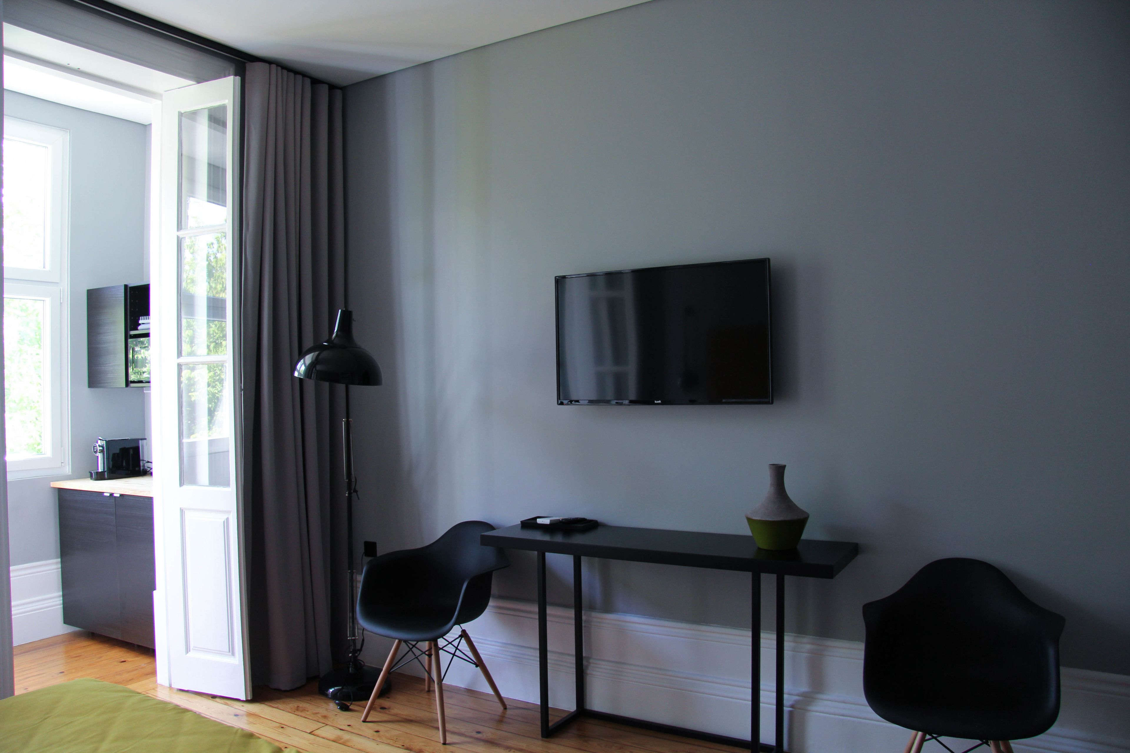 A modern room with a flat-screen TV mounted on the wall, a small table with a vase, two black chairs, and a wooden floor.
