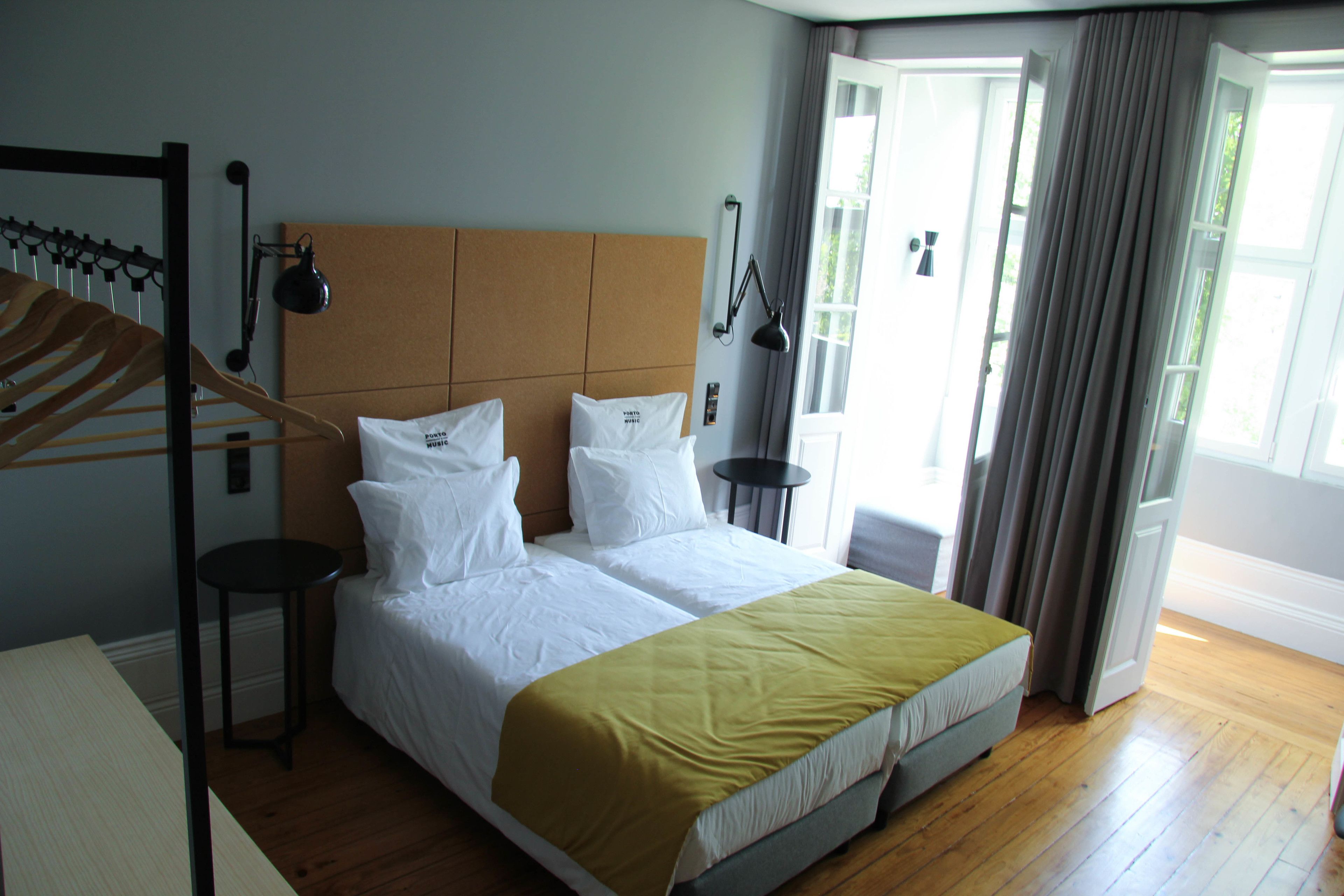 Une chambre d’hôtel avec un grand lit, un plancher en bois, une tête de lit, une petite table et une fenêtre avec des rideaux.