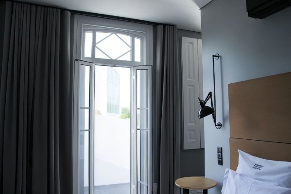 A hotel room with a bed, a bedside table, a lamp, and a view through a door.