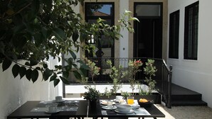 A table set for breakfast with plates, cups, and a bowl of fruit, surrounded by chairs, in a courtyard with a white building and black railings in the background. - Porto Music Guest House (Porto)