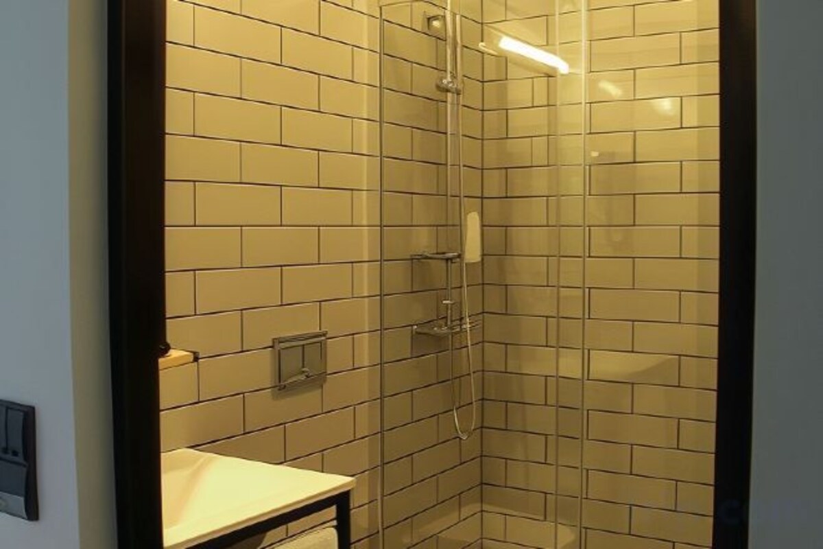 A corner bathroom with a glass-enclosed shower, tiled walls, and a small sink.