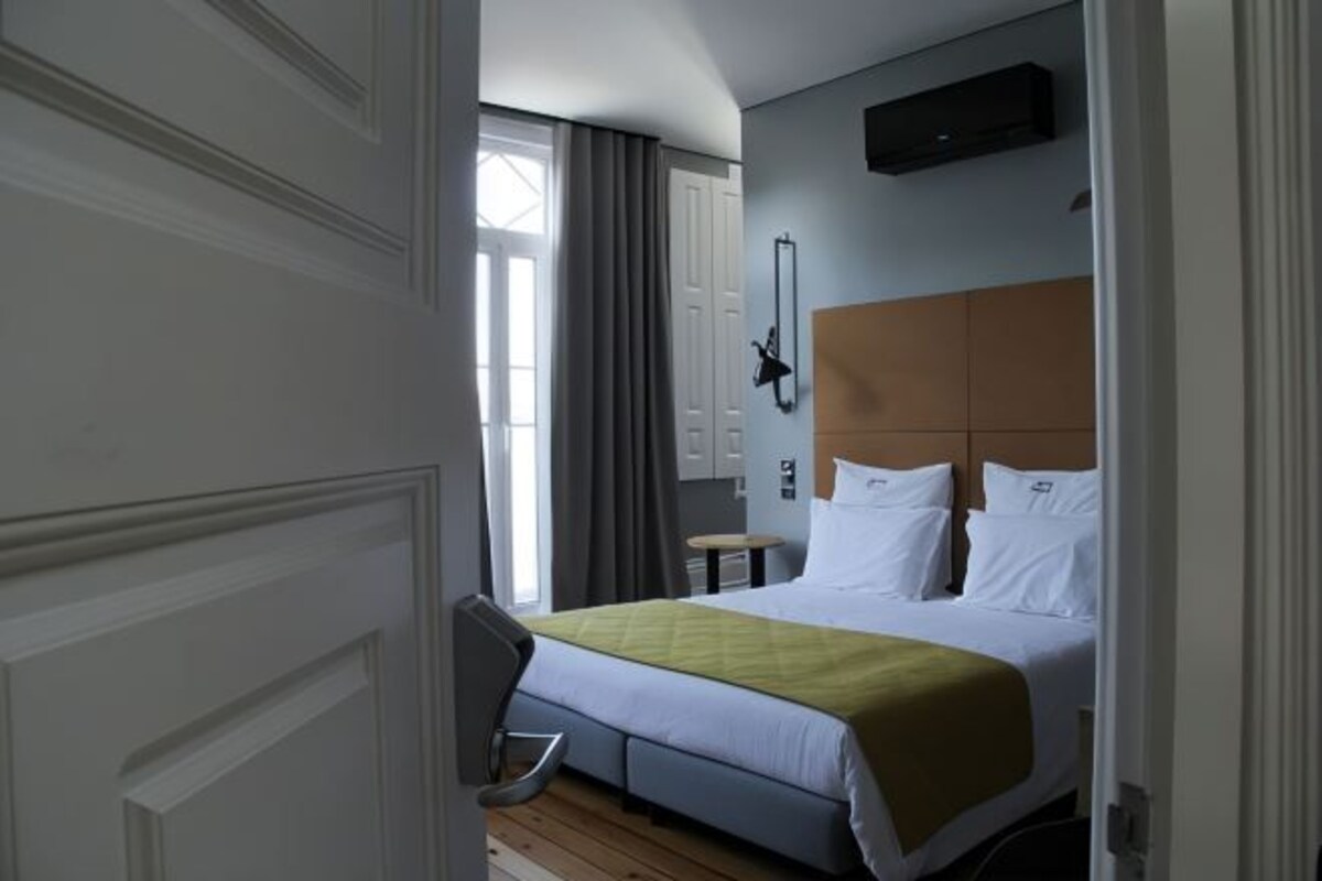 A hotel room with a bed, a bedside table, a chair, and a window with curtains.