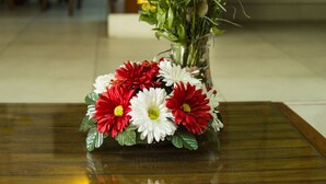Un vase rempli de différentes sortes de fleurs est posé sur une table dans une pièce où se trouve un escalier et une lampe fixée au mur.