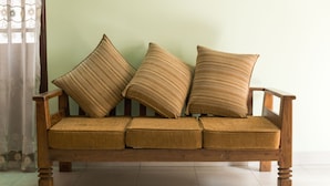 Un canapé en bois avec trois coussins, placé contre un mur de couleur vert clair.