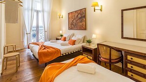 A hotel room with two beds, a desk, a chair, a mirror, and a painting on the wall. - Flores 105 Guesthouse (Lisbon)