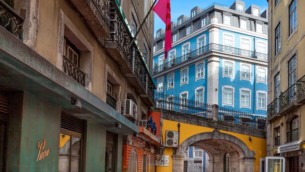 An outdoor café with tables and chairs, a flag, and buildings with balconies. - Flores 105 Guesthouse (Lisbon)