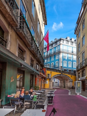 An outdoor café with tables and chairs, a flag, and buildings with balconies. - Flores 105 Guesthouse (Lisbon)