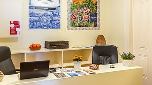 A reception desk with a laptop, a bowl of oranges, a box labeled "ANTONIO," and a potted plant. - Flores 105 Guesthouse (Lisbon)