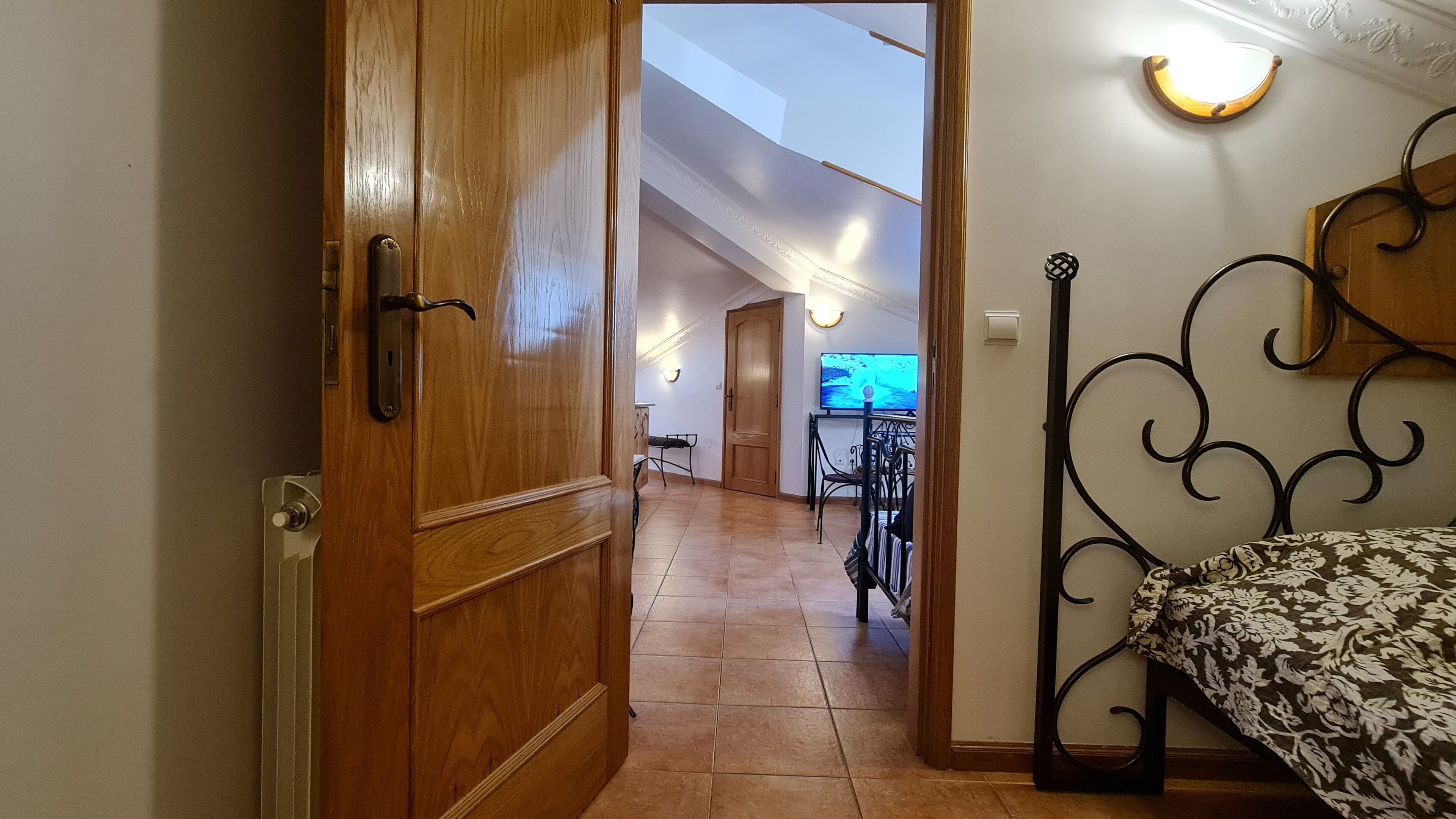 Un couloir avec une porte en bois, un lit recouvert d’une couvre-lit à motifs et un coin repas avec une table et des chaises.