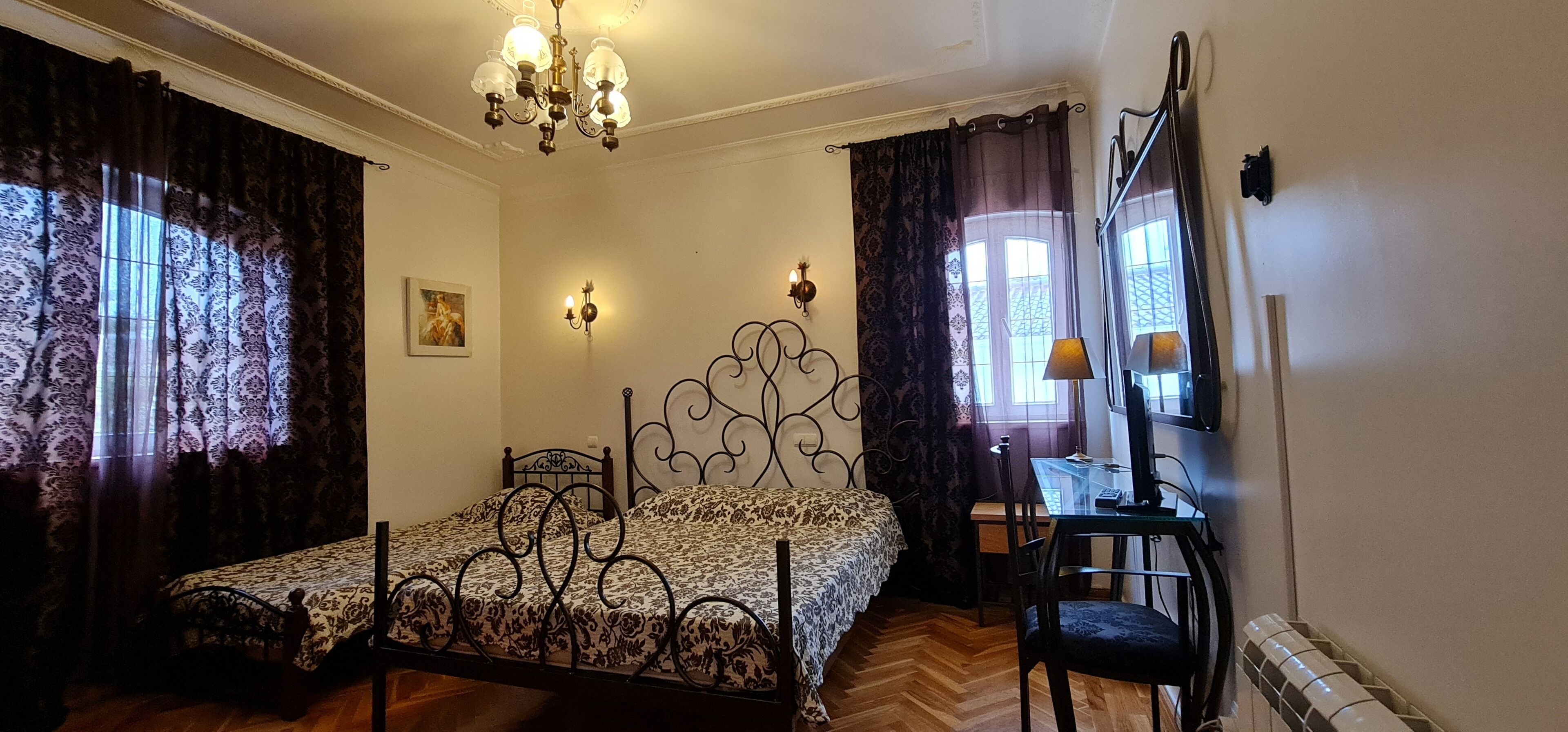 A bedroom with a bed, a desk, a chair, a chandelier, and a window with curtains.