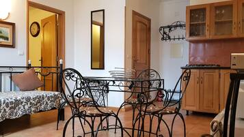 Un espacio habitable compacto con cama, una mesa de comedor con sillas, una zona de cocina con armarios de madera y un espejo montado en la pared.