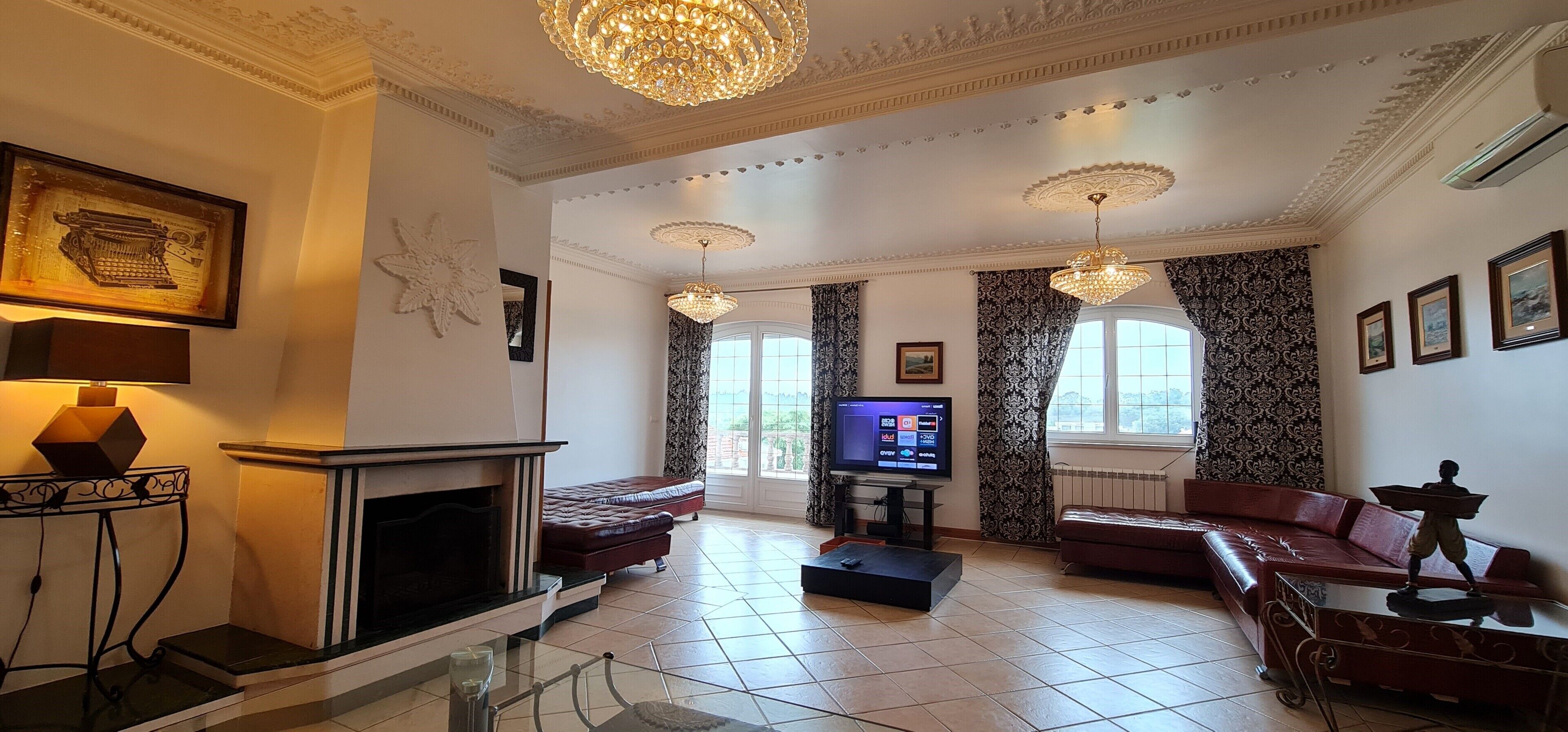 A spacious living room with a fireplace, leather sofas, a television, and decorative lighting.