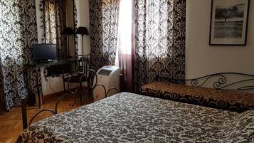 Une chambre avec un lit, un bureau avec un ordinateur et des rideaux à motifs floraux.