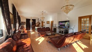 A spacious living room with a brown leather sofa, a glass coffee table, and a TV. - Silver Village Residence (Leiria)