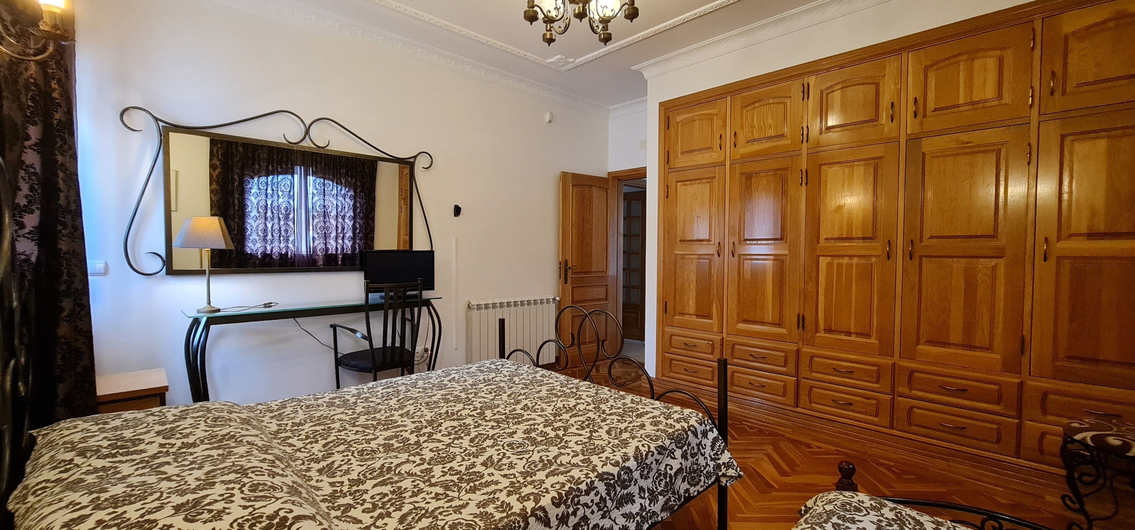 A bedroom with a bed, a desk with a chair, a large mirror, and a wardrobe.