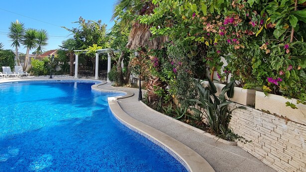 A swimming pool with a curved edge, surrounded by a stone wall and lush greenery. - Silver Village Residence (Leiria)