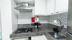 A kitchen with a gas stove, a coffee maker, and a red kettle on the countertop. - Flats no Carneiros Beach Resort (Tamandaré)