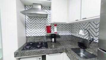 Una cocina con estufa a gas, cafetera y tetera roja en la encimera.