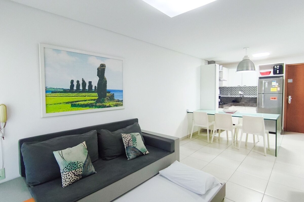 A modern living room with a black sofa, a glass dining table, and a kitchen in the background.