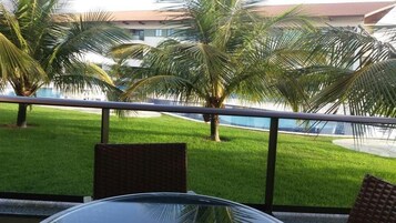 Un balcón con vista a una piscina, palmeras y un edificio al fondo.