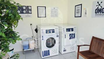 Uma área de lavanderia com duas máquinas de lavar, um banco e cartazes informativos na parede.