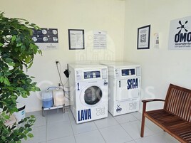 Un área de lavandería con dos lavadoras, un banco y carteles informativos en la pared.