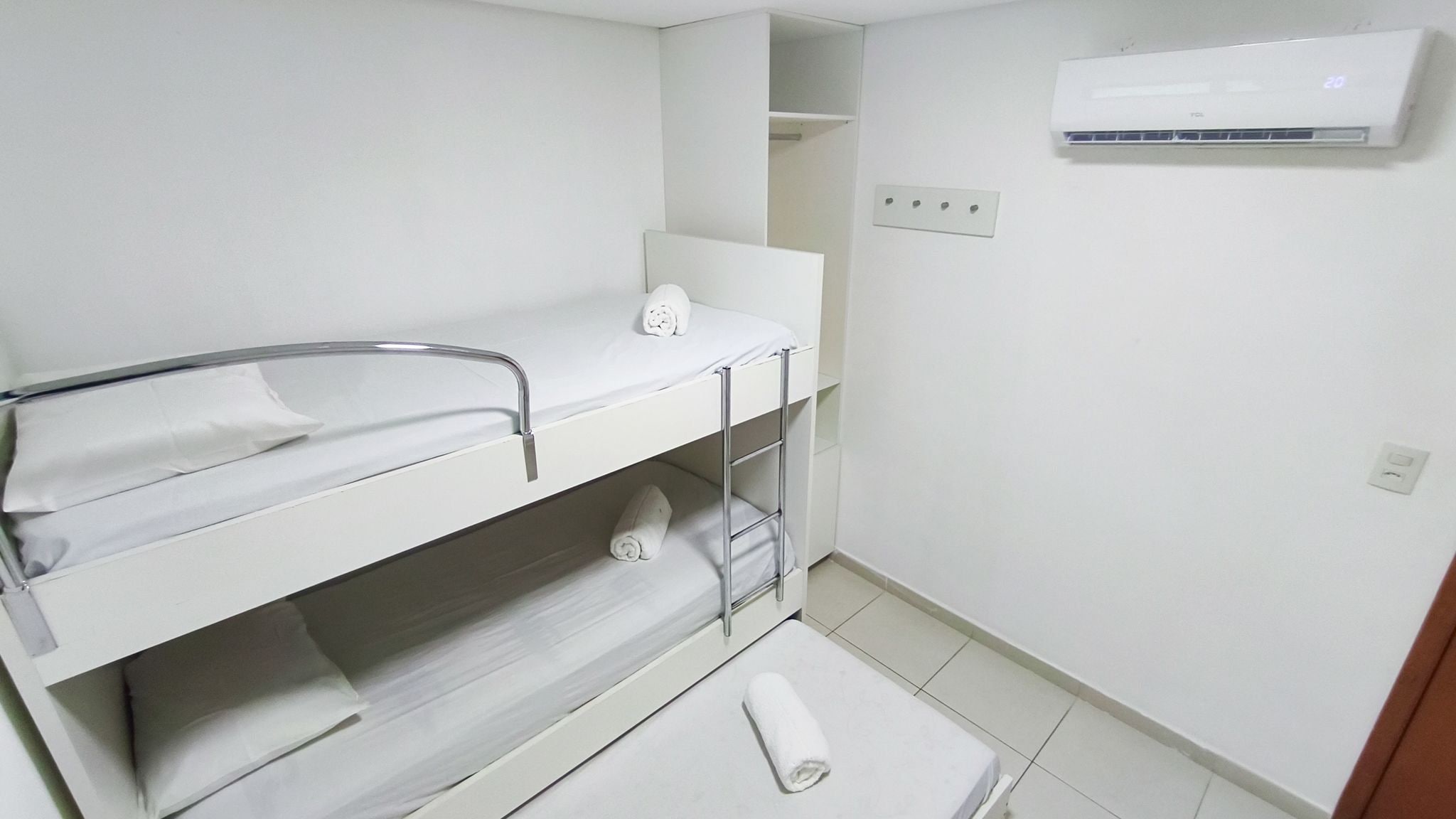 A small, clean room with a bunk bed, a sink, and an air conditioning unit.