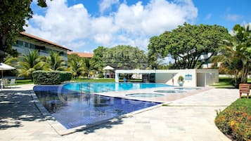 A swimming pool with a tiled deck, surrounded by palm trees and a building with a red roof.