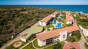 Vista aèria d'un complex turístic amb diversos edificis, una gran piscina i vistes a l'oceà.