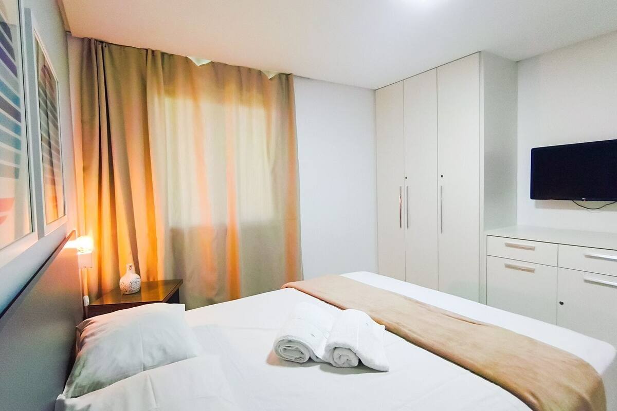 A hotel room with a bed, a TV, a wardrobe, and a nightstand with a lamp.