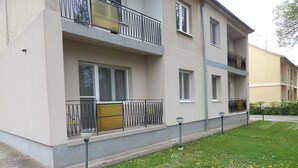 A multi-story residential building with balconies, a paved sidewalk, and a grassy area with flowers. - Hajdu Vendeghaz (Hajduszoboszlo)