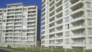 A multi-story residential building with balconies, a fenced area, and a clear sky. - Departamento Mar Serena 6 (La Serena)
