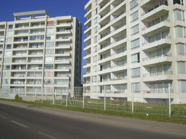 Un edificio residencial de varios pisos con balcones, un área cercada y cielo despejado.