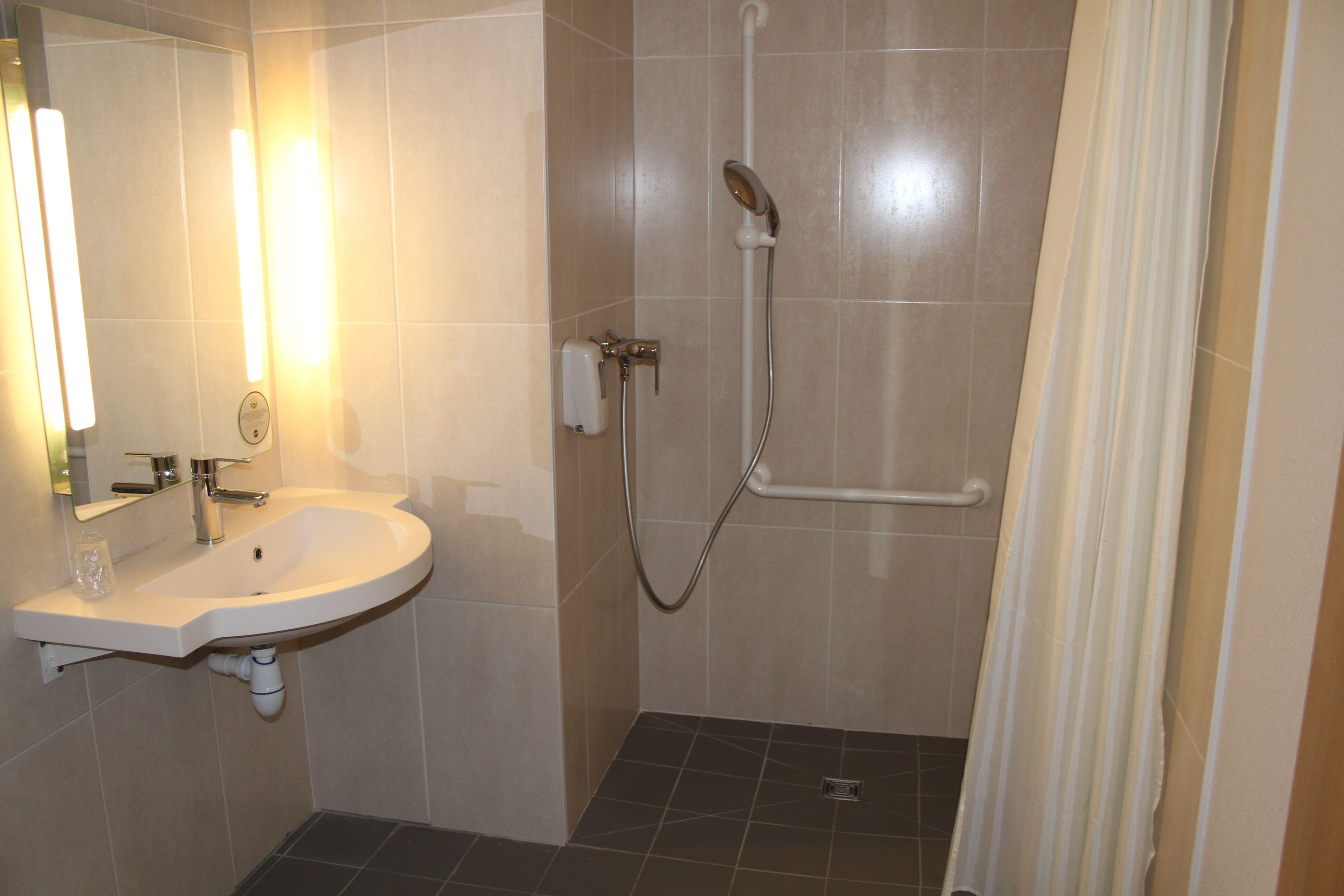 Ein Badezimmer mit Waschbecken, Spiegel, Dusche und Handtuchhalter.