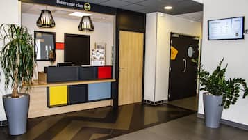 Un área de recepción con mostrador, plantas en macetas y un panel informativo en la pared.