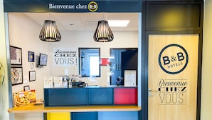 A reception desk with a sign reading "Bienvenue chez B&B Hotels" and a wooden door with the same sign.