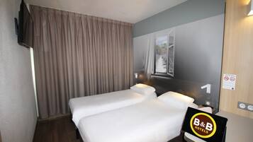 A hotel room with two beds, a TV mounted on the wall, a window with curtains, and a sign indicating the room number.