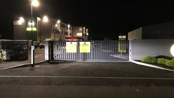 A gated parking area at night with illuminated street lamps and a building in the background.