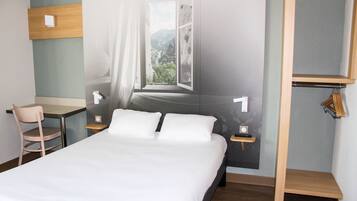 A hotel room with a bed, a desk, a chair, and a view of a mountain through a window.