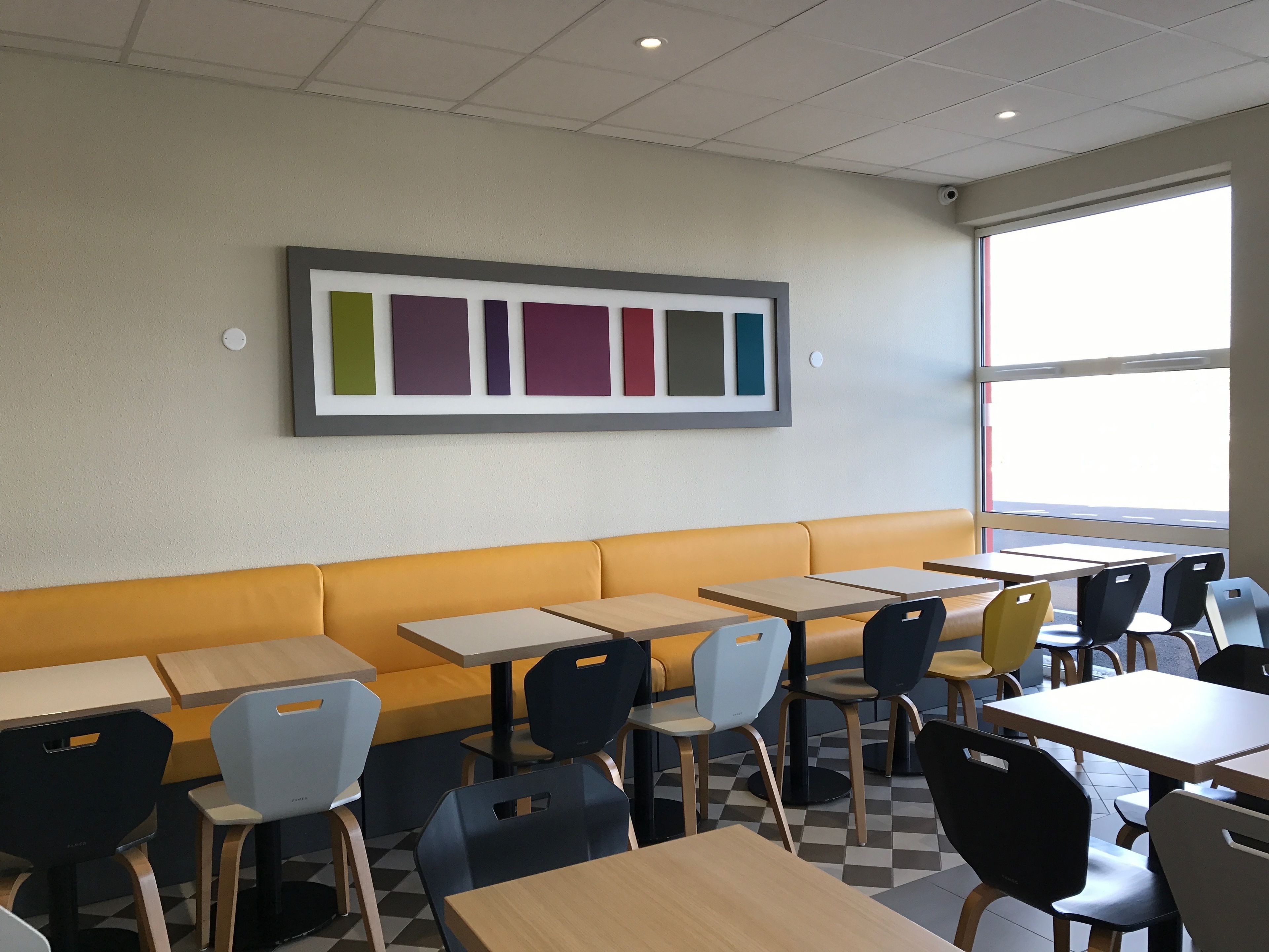 Un interior de restaurante con suelo a cuadros, asientos en cabinas amarillos y una paleta de colores montada en la pared.