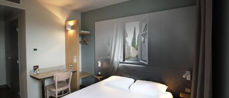 A hotel room with a bed, a desk, a chair, a nightstand, and a wall-mounted shelf.
