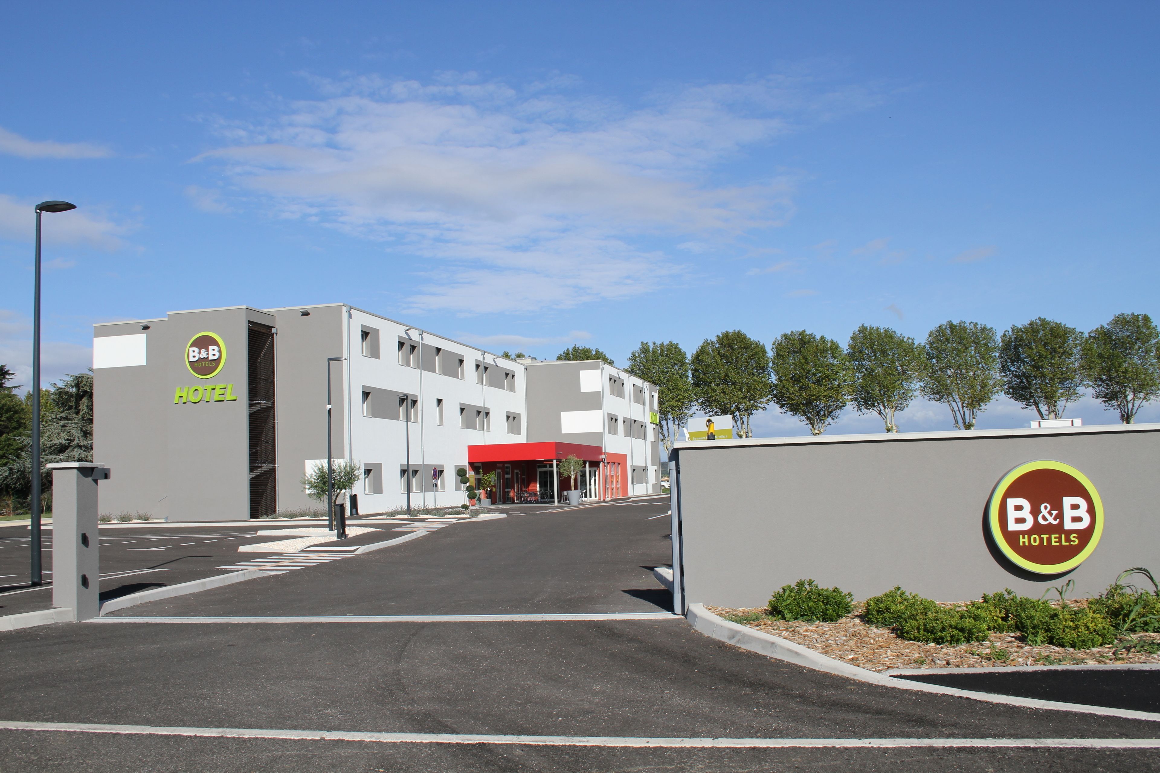 A B&B hotel with a modern design, featuring a red entrance and a parking lot.