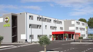 A modern hotel with a red entrance, multiple floors, and a parking lot.