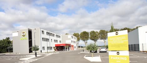 A hotel with a red entrance, a parking sign indicating video surveillance, and a clear sky.