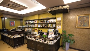 A reception area with a dark wooden counter, shelves with various items, a potted plant, and a framed artwork on the wall. - Hotel Victoria (Tirana)