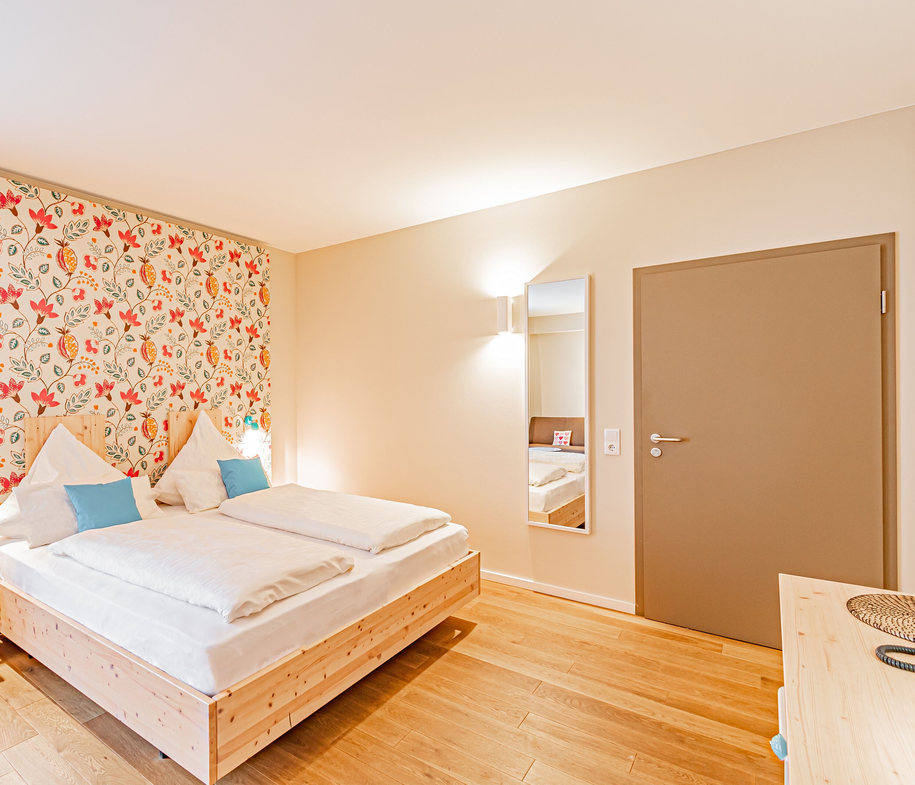 A bedroom with a wooden bed, a floral wallpaper, a mirror, and a door.