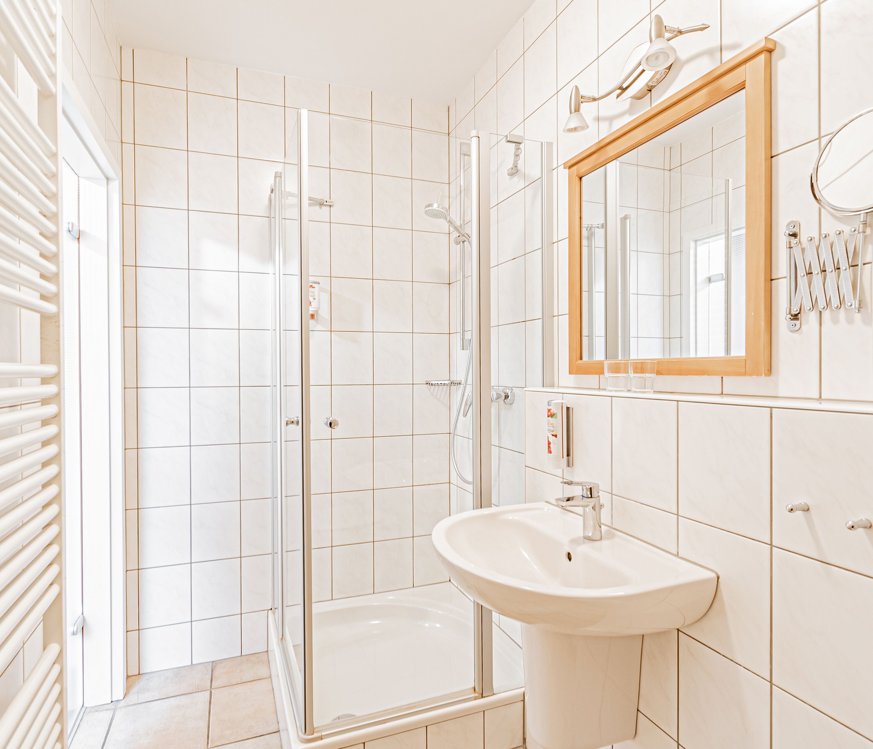 Un baño moderno con cabina de ducha de vidrio, un lavamanos blanco y un espejo con marco de madera.