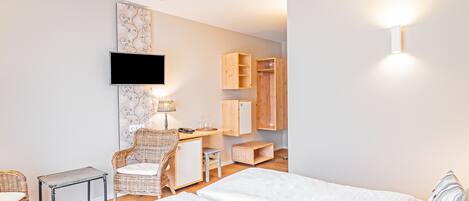 A hotel room with a bed, a desk, a chair, a TV, and a wardrobe.