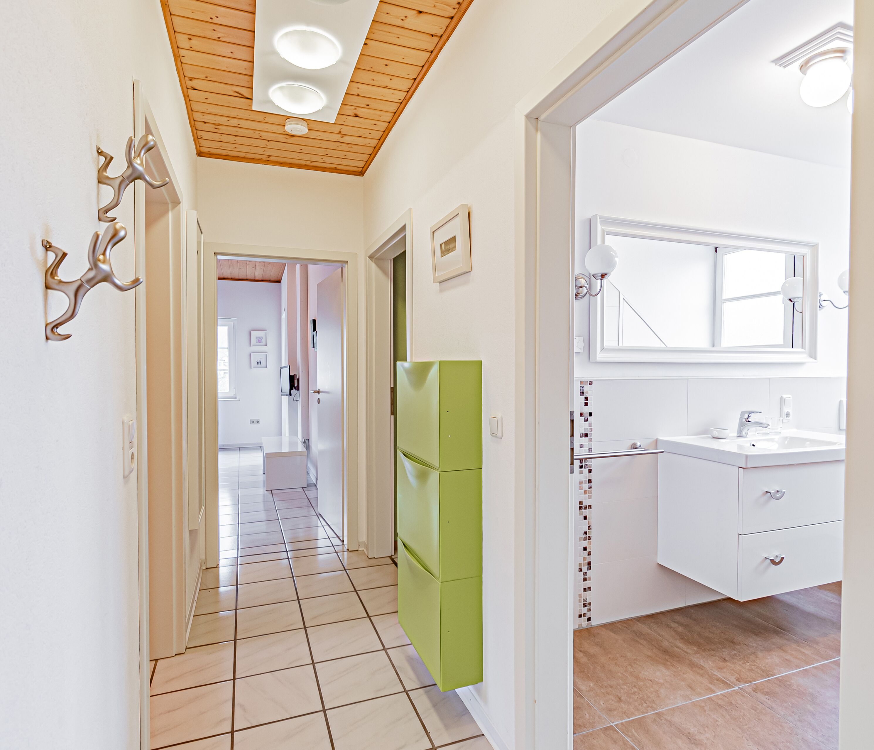 Un corridoio con una porta verde che conduce a un bagno con un lavandino e uno specchio bianchi.